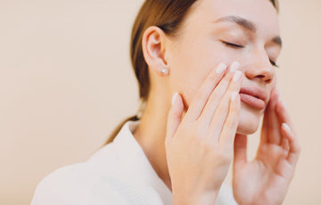 A serene woman gently massages her cheeks with both hands, eyes closed, conveying relaxation.
