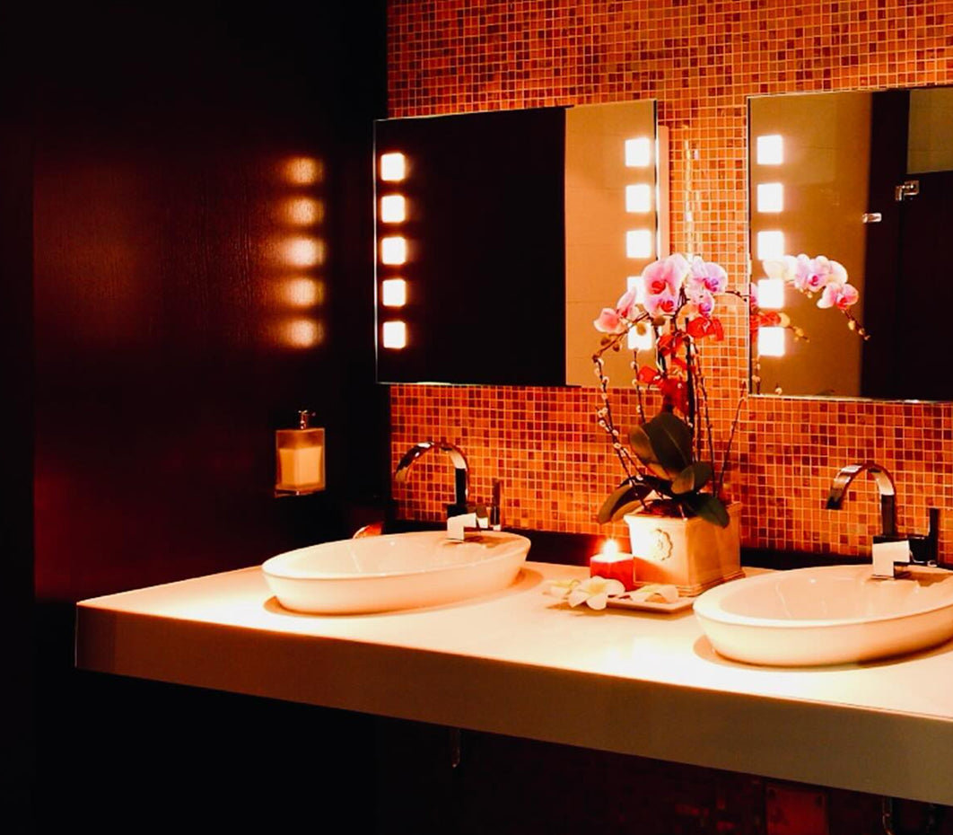 Luxurious bathroom with warm lighting, featuring two oval sinks, a mirrored wall with lit panels, and an orchid centerpiece. Elegant and serene ambiance.