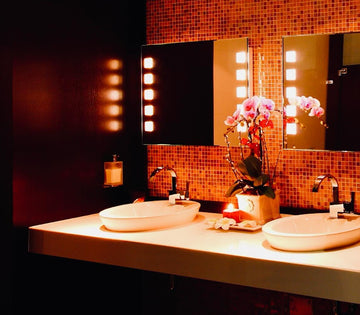 Luxurious bathroom with warm lighting, featuring two oval sinks, a mirrored wall with lit panels, and an orchid centerpiece. Elegant and serene ambiance.